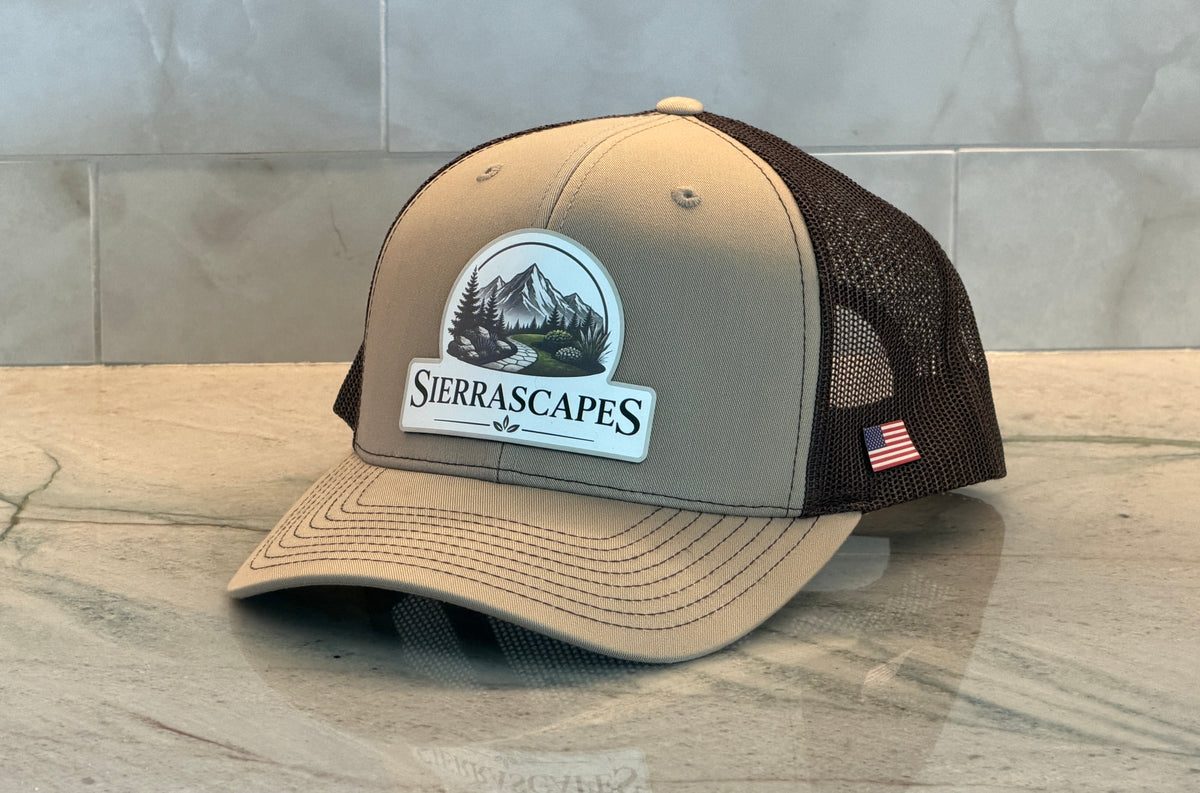 A brown trucker at with a white full color printed leather patch with an outdoor mountain landscape logo and the word Sierrascapes.