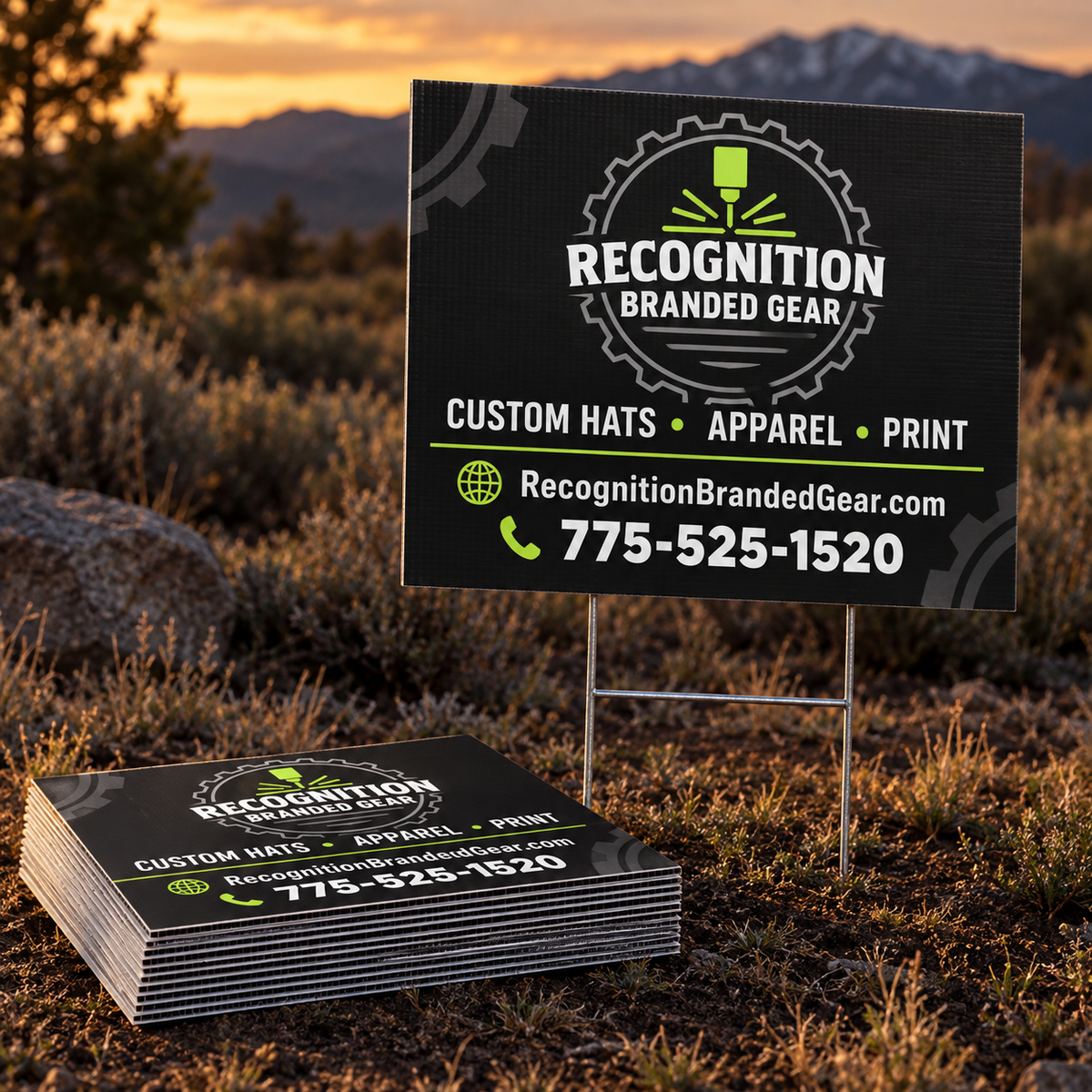 Custom printed coroplast yard sign and a stack of matching signs for 'Recognition Branded Gear' displayed outdoors in a grassy field at sunset, with mountains in the background.