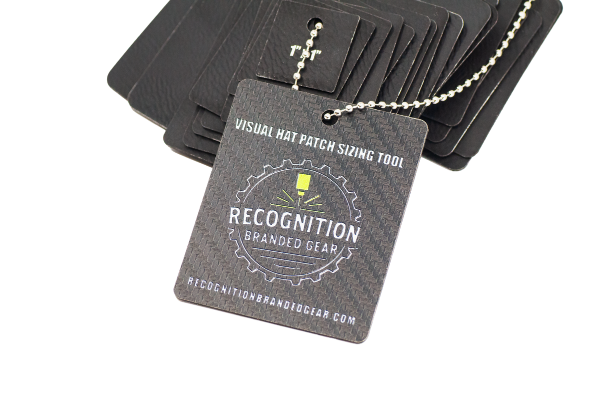 A black rectangular hat patch sizing tool card with a silver ball chain, shown in front of a stack of matching black cards on a white background. The front card reads 'VISUAL HAT PATCH SIZING TOOL' and 'RECOGNITION BRANDED GEAR'.