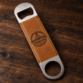 A personalized bottle opener with a brown leather handle and silver metal ends, featuring an engraved 'Recognition Branded Gear' logo, resting on a dark wood background.