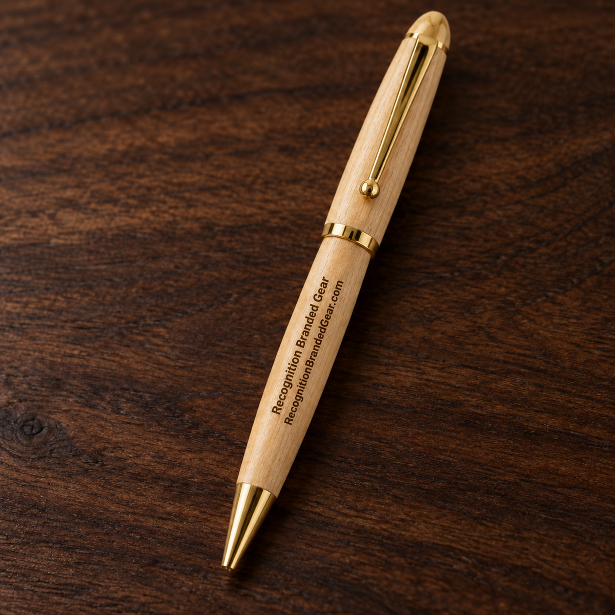 A personalized wooden pen with gold metal accents and engraved text, resting diagonally on a dark brown wood grain surface.