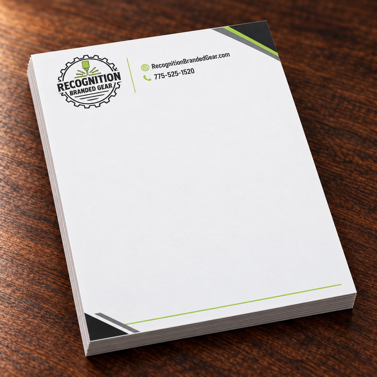 A stack of white branded letterhead on a dark wood tabletop. The top page shows the Recognition Branded Gear logo and contact details in black and lime green, with dark gray corner accents.