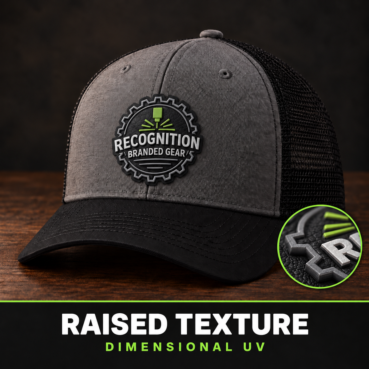 A dark gray and black trucker cap with a raised circular 'Recognition Branded Gear' patch on the front, shown on a dark wood surface against a dark background. A circular inset at the bottom right highlights the raised texture effect, and text at the bottom reads 'RAISED TEXTURE DIMENSIONAL UV'.