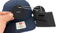 A navy blue baseball cap with a white and red Richardson 0SFM patch on the front, shown alongside black leather hang tags and sizing cards. A hand is holding one of the black leather hang tags on a silver ball chain against a plain white background.