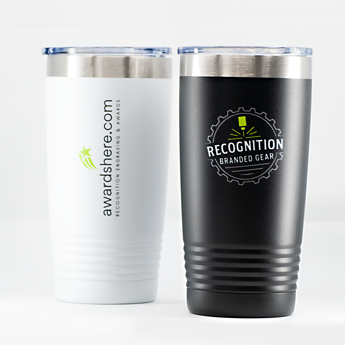 Two insulated travel tumblers on a light gray studio background. The left tumbler is white with a silver lid and printed vertical text reading awardshere.  The right tumbler is black with a silver rim and printed with a logo reading Recognition Branded Gear.