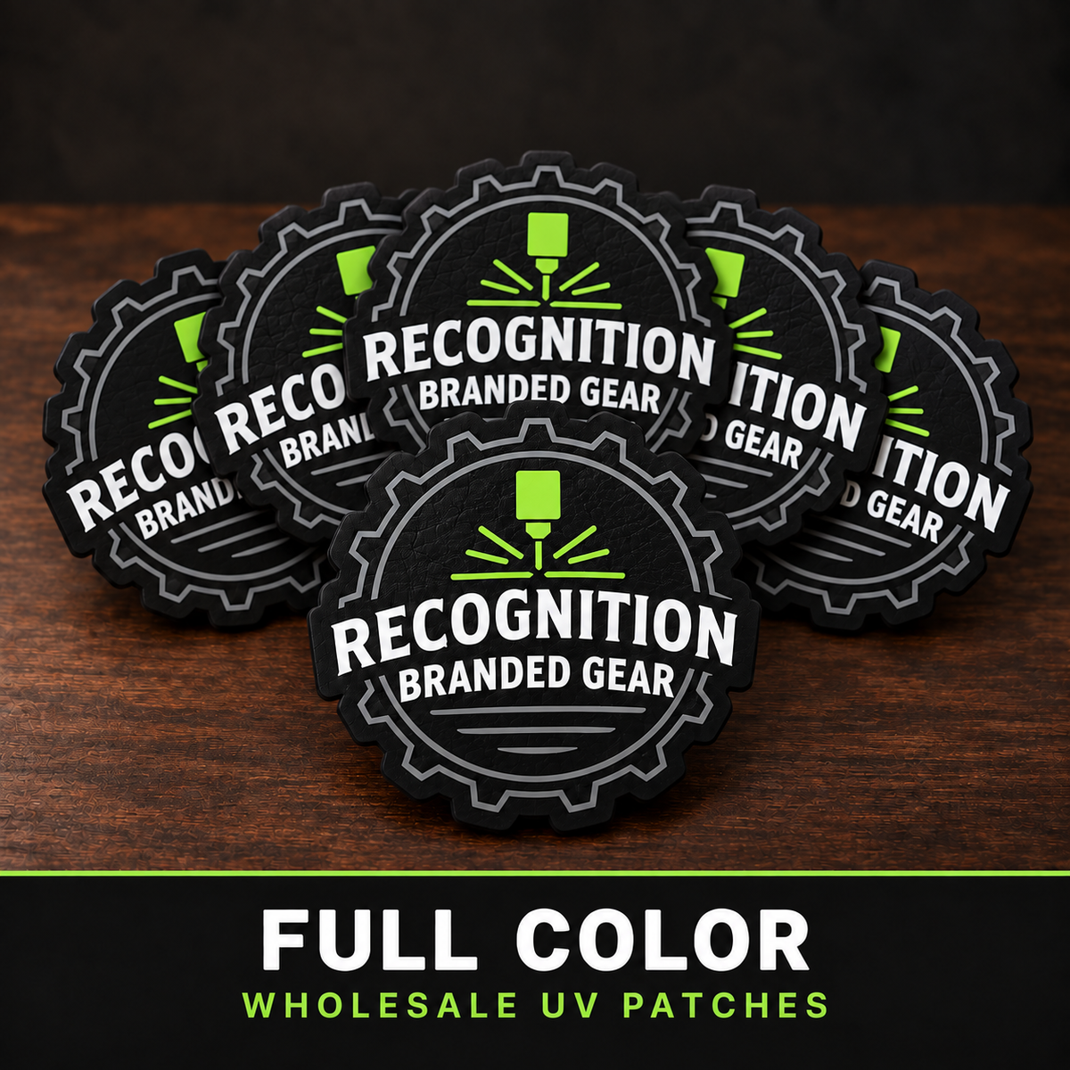 Five circular black and gray branded patches with white text reading 'Recognition Branded Gear' and a bright green logo, arranged on a dark wood surface. A black banner at the bottom reads 'FULL COLOR WHOLESALE UV PATCHES.